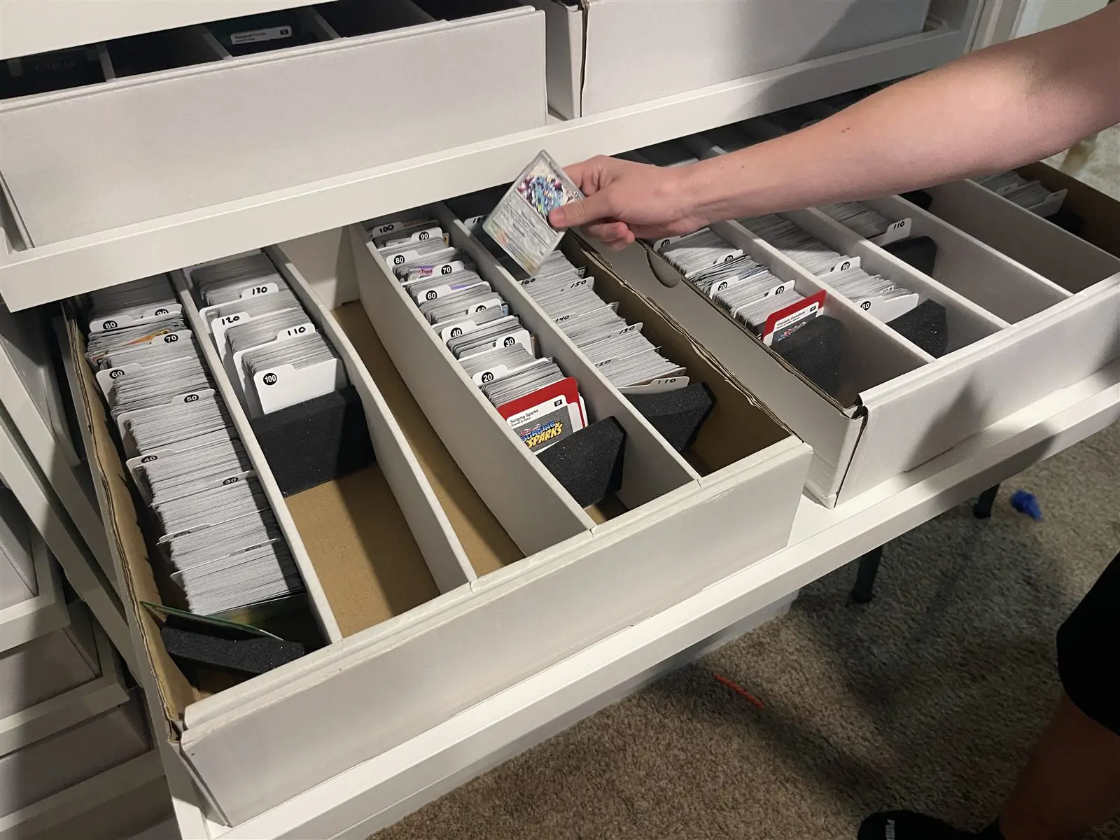 A drawer of sorted Pokemon cards with a hand pulling one out